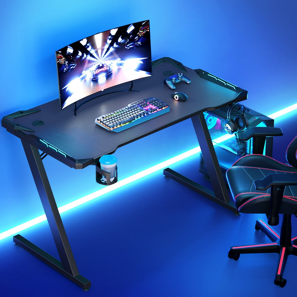 Artiss 120cm RGB gaming desk lifestyle shot with blue under-desk lighting, monitor and gaming chair