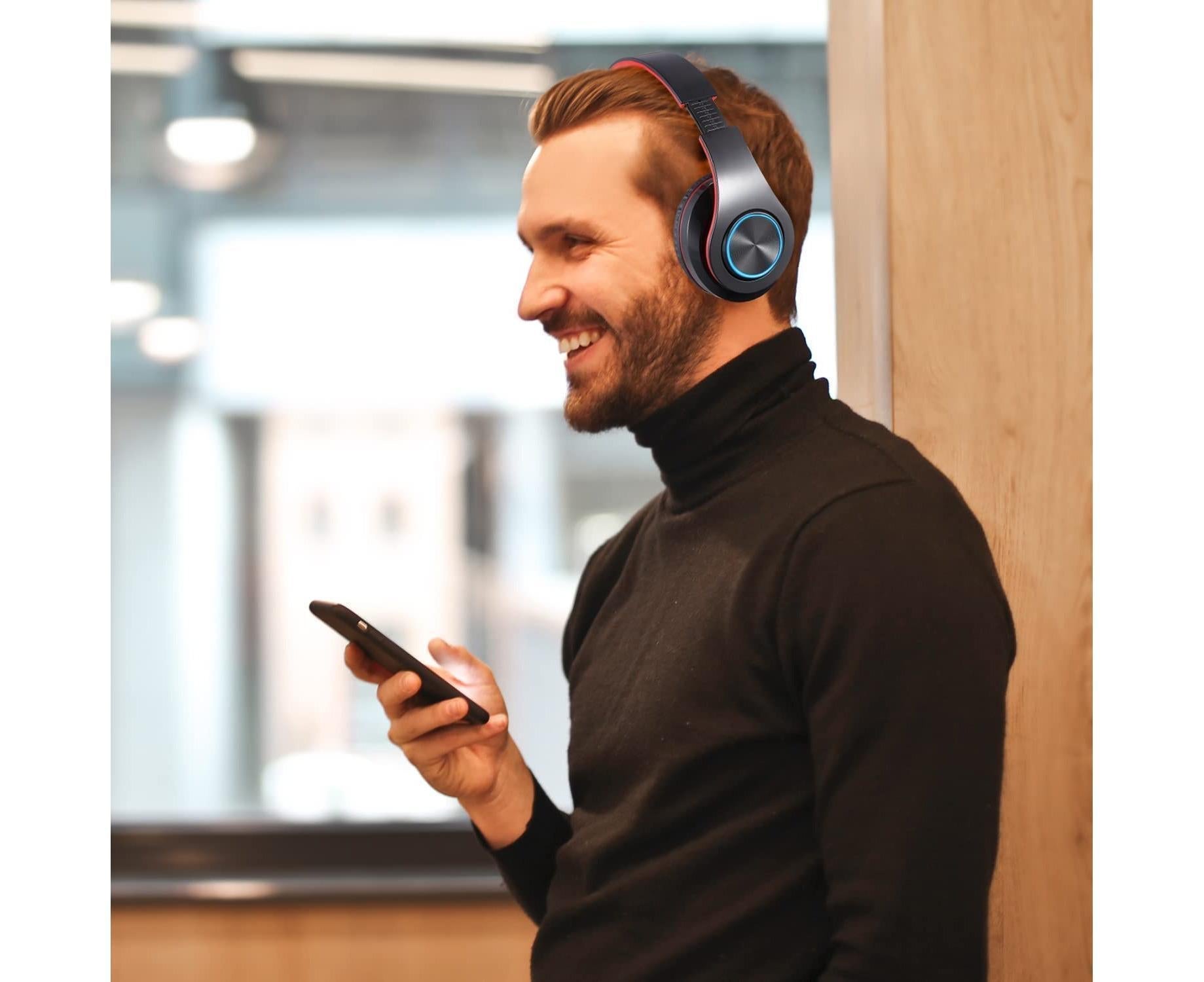 Man in black turtleneck wearing JX-992 Bluetooth headphones, holding phone in a bright cafe